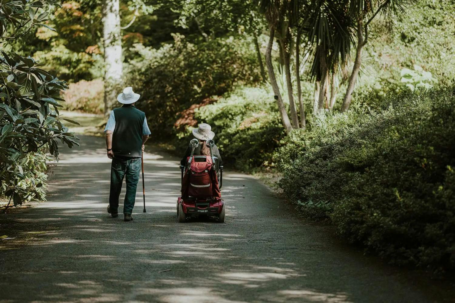 Old couple with cane and mobility scooter in park